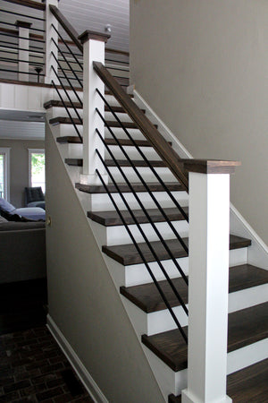 A modern staircase showcases dark wooden steps, white risers, and a sleek Holmes 7800 red oak handrail. The railing includes slim horizontal metal rods on white posts, leading upward in a residential space with light walls.